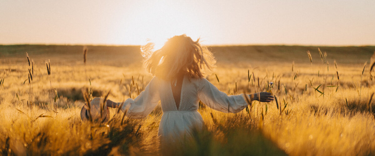 young beautiful woman with long blond hair in a white dress on a wheat field in the early morning at sunrise. Summer is the time for dreamers, flying hair, a woman running across the field in the rays of the sun. travels